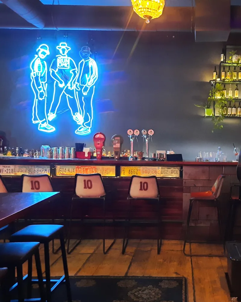 Bar counter with a neon sign and stools at Rudeboy Bar