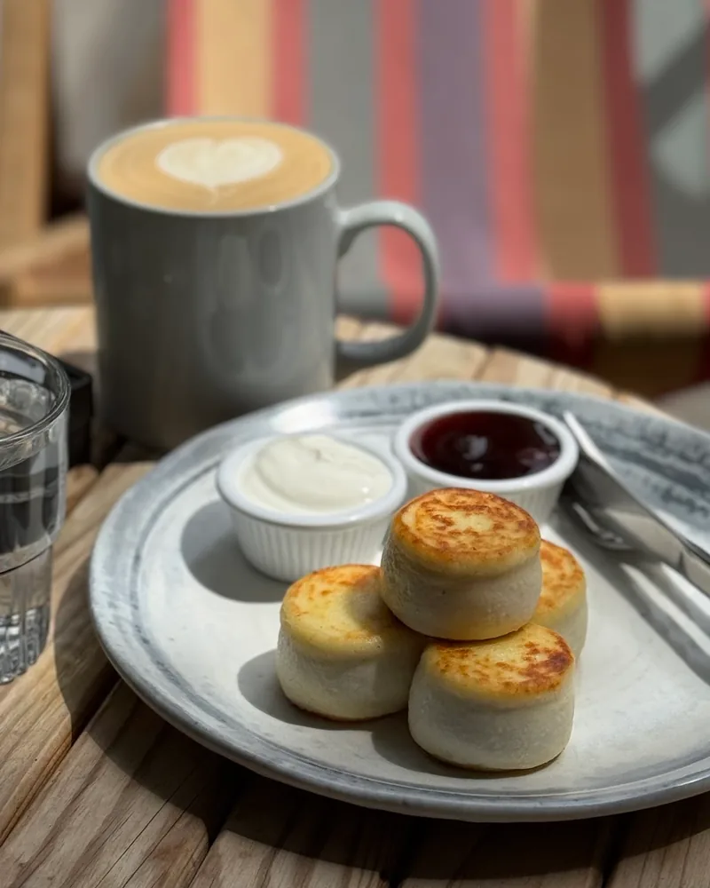 Syrniki with sour cream and jam next to a latte at Sali Coffee
