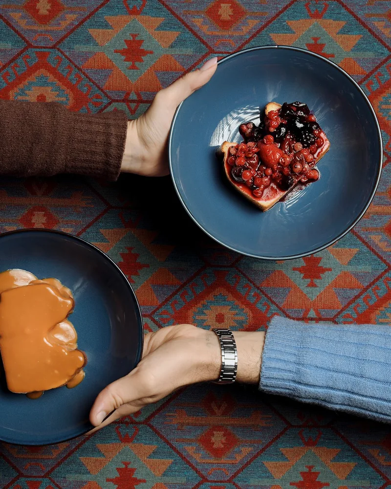 Two bowls of desserts held by hands over patterned carpet at Samsara