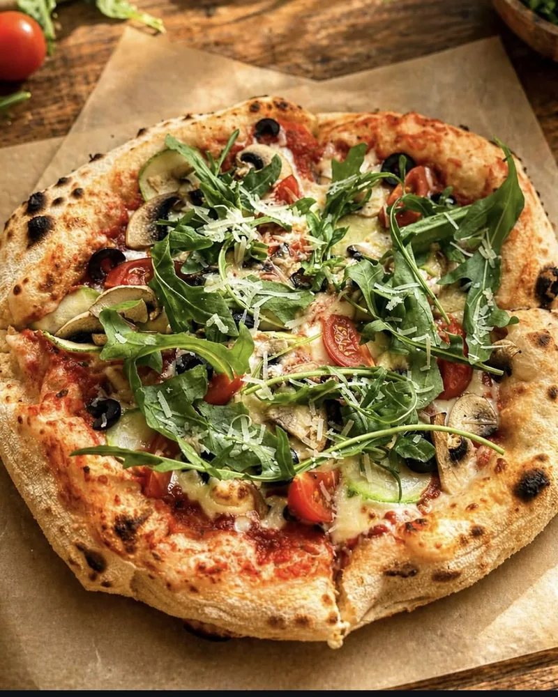 Pizza topped with arugula, tomatoes, mushrooms, and zucchini at Savora