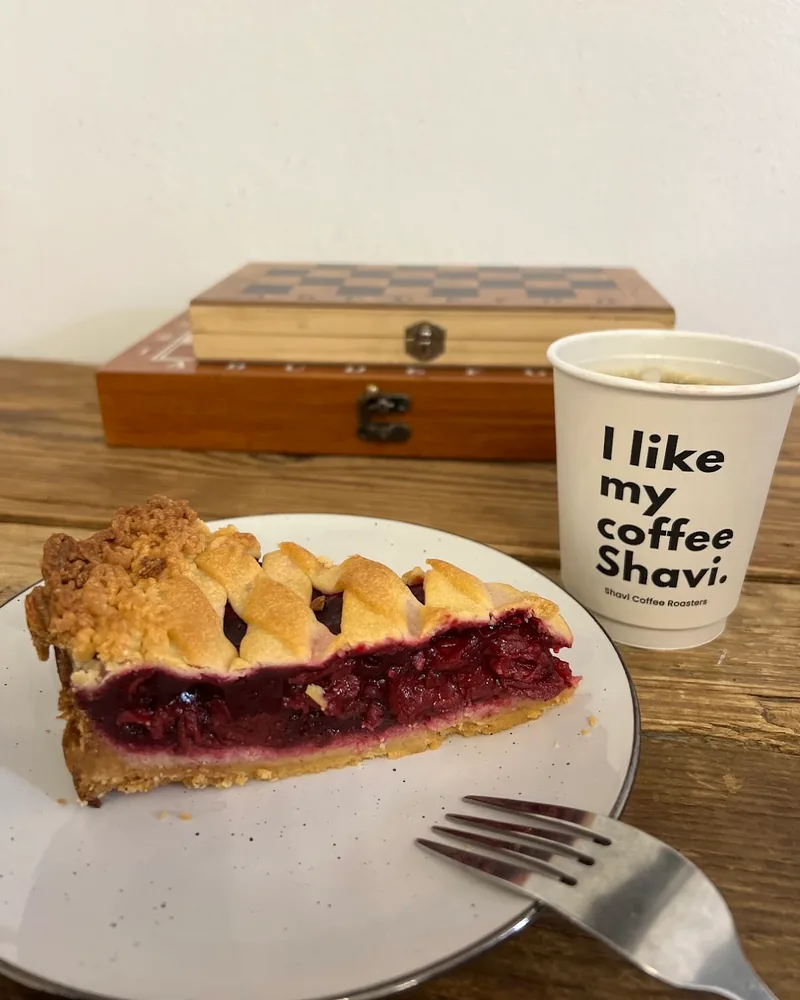Slice of cherry pie on a plate beside a paper coffee cup at Shavi Coffee Roasters