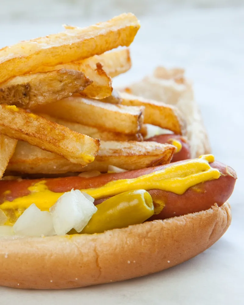 Hot dog topped with french fries and mustard at Shawarmaniac