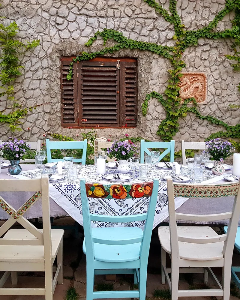 Outdoor table set with painted wooden chairs and stone wall backdrop at Sheen Aura