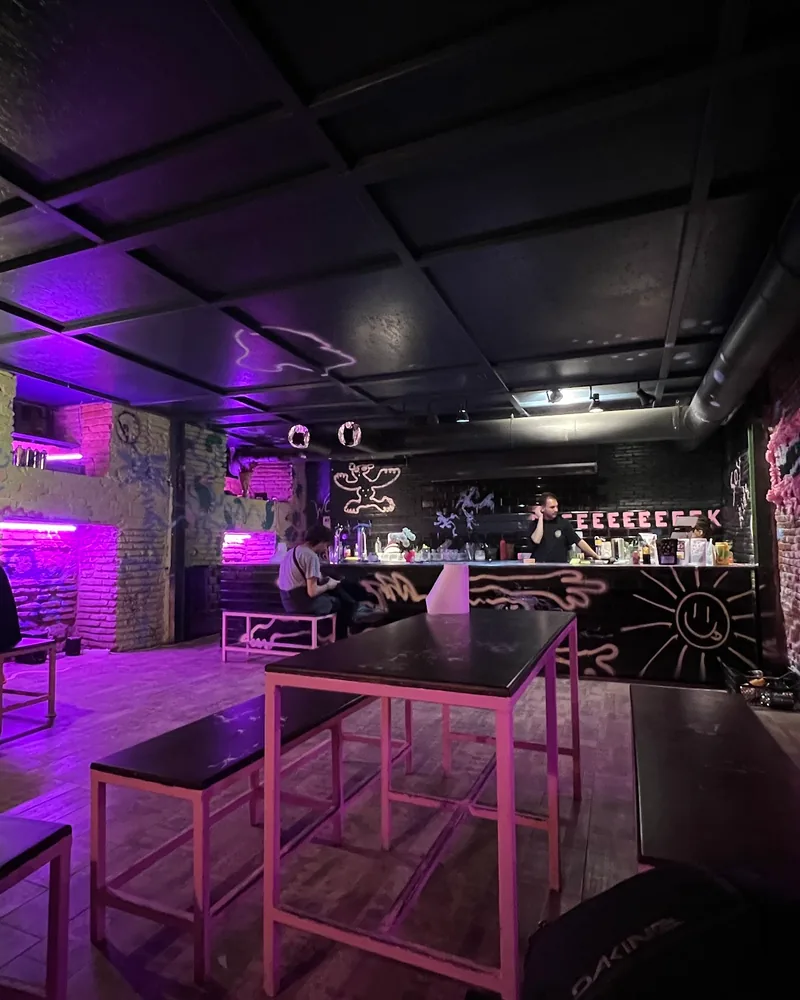 Underground bar seating with neon lighting and painted brick walls at Shpana