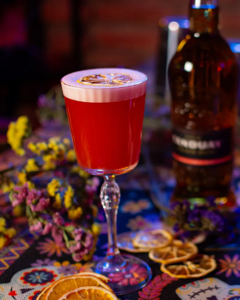 Red cocktail with foam and dried citrus wheel garnish at So Lucky Cocktail Bar