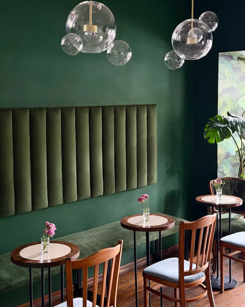 A dark green room with a velvet banquette, small round tables and glass bubble lamps at Soda