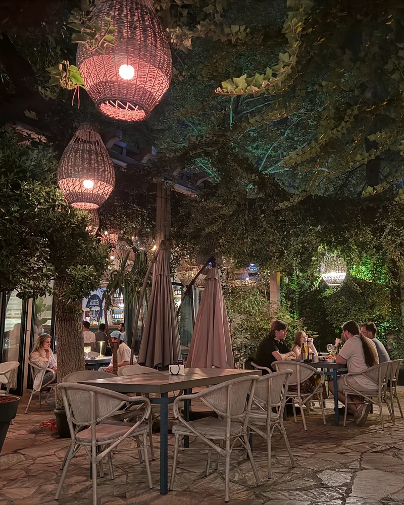Leafy courtyard terrace with wicker pendant lamps and dining tables at Sormoni