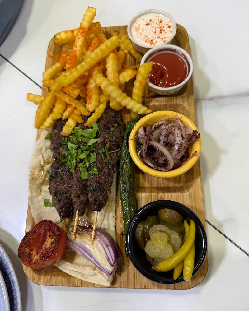 Kebab platter with fries, sauces and pickles on a wooden board at Station 1984