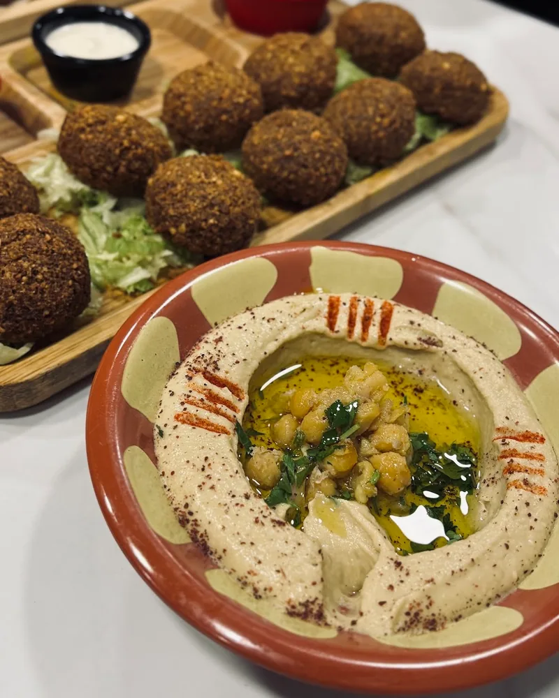 Hummus plate with chickpeas and olive oil beside a falafel platter at Station 1984