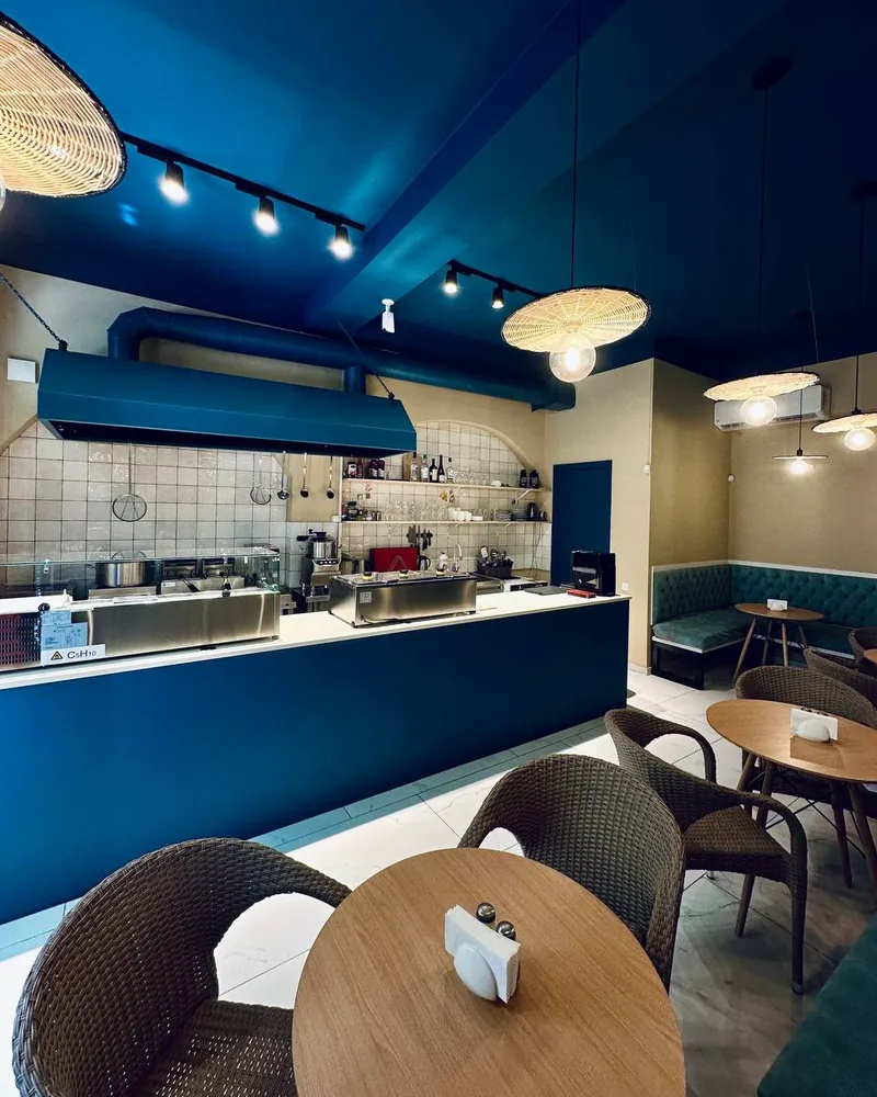 Dining area and service counter with blue ceiling and woven pendant lamps at Supra Hummus