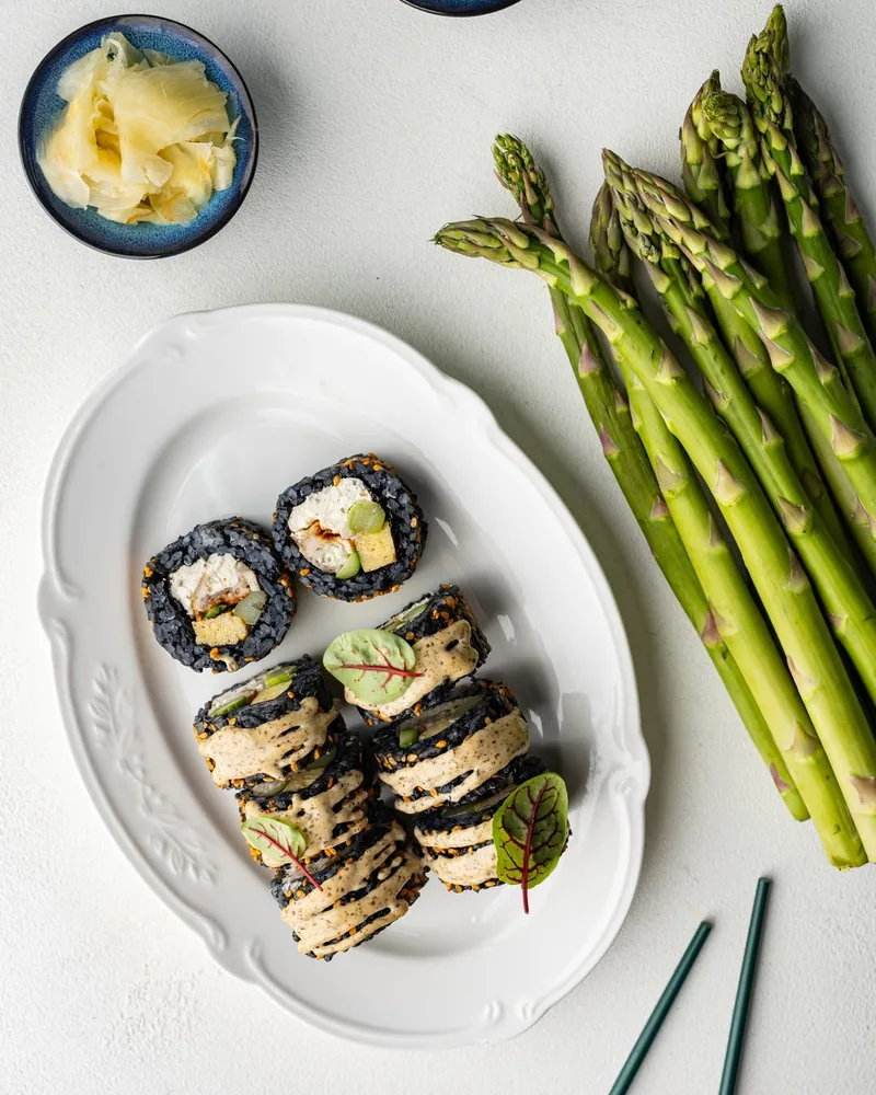 Sushi rolls with black rice on a white platter with asparagus and ginger at Sushi Icons