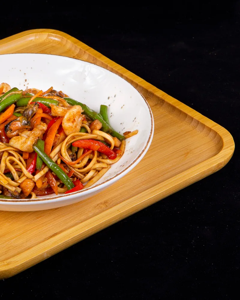 Stir-fried noodles with shrimp and vegetables in a white bowl at Sushi Rolls