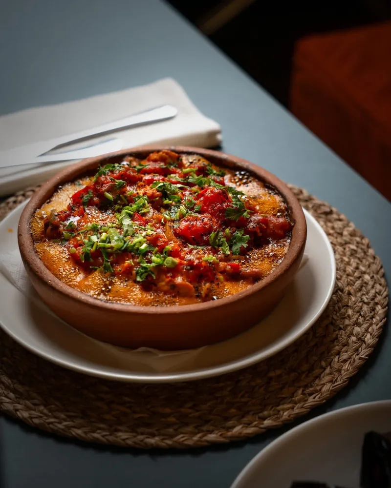 Baked dish with herbs in a clay pot on a woven placemat at Tbili Kera