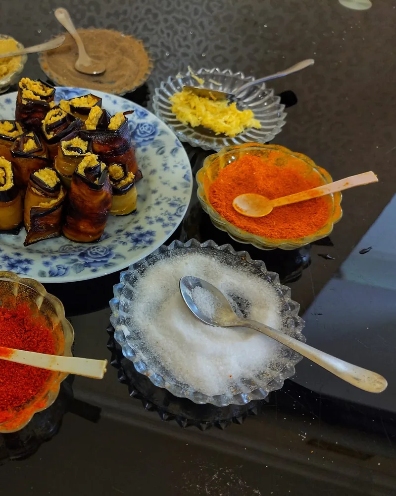 Aubergine rolls with a walnut filling on a blue floral plate beside small glass bowls of ground red pepper, salt and other spices at Tbilisi Cooking Class