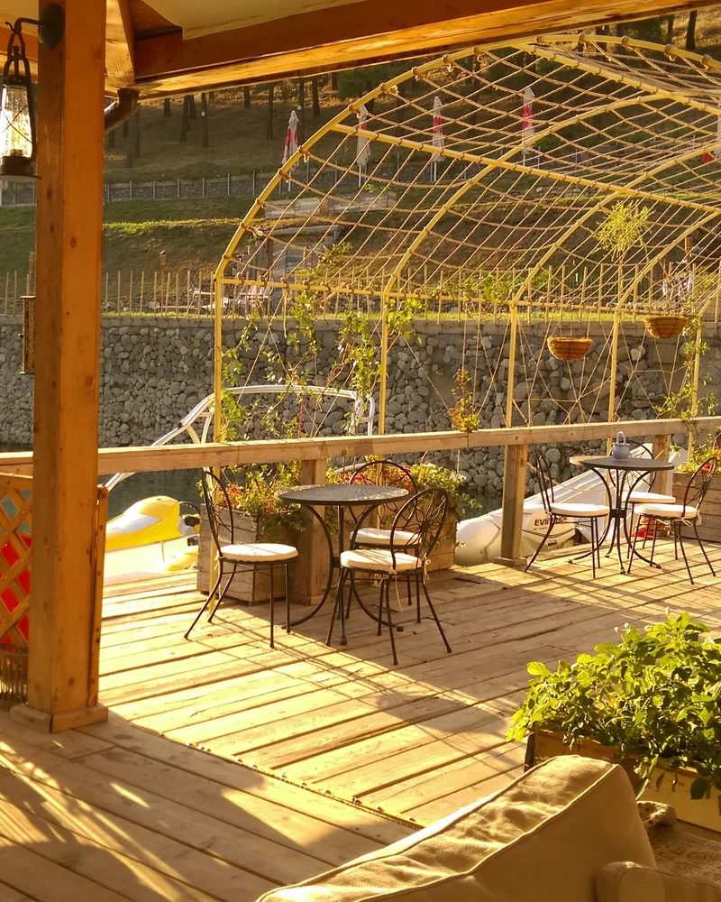 Wooden lakeside terrace with wire trellis and cafe tables at La Cote