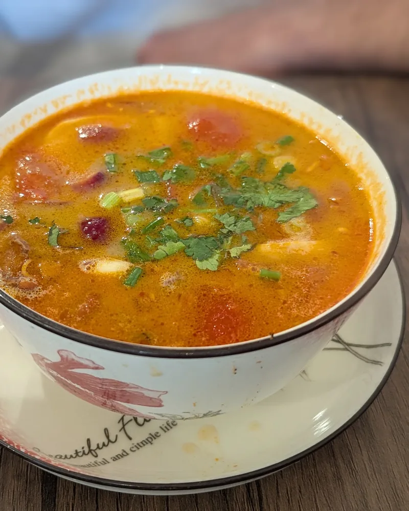 Bowl of tom yum soup garnished with herbs at Thanapon