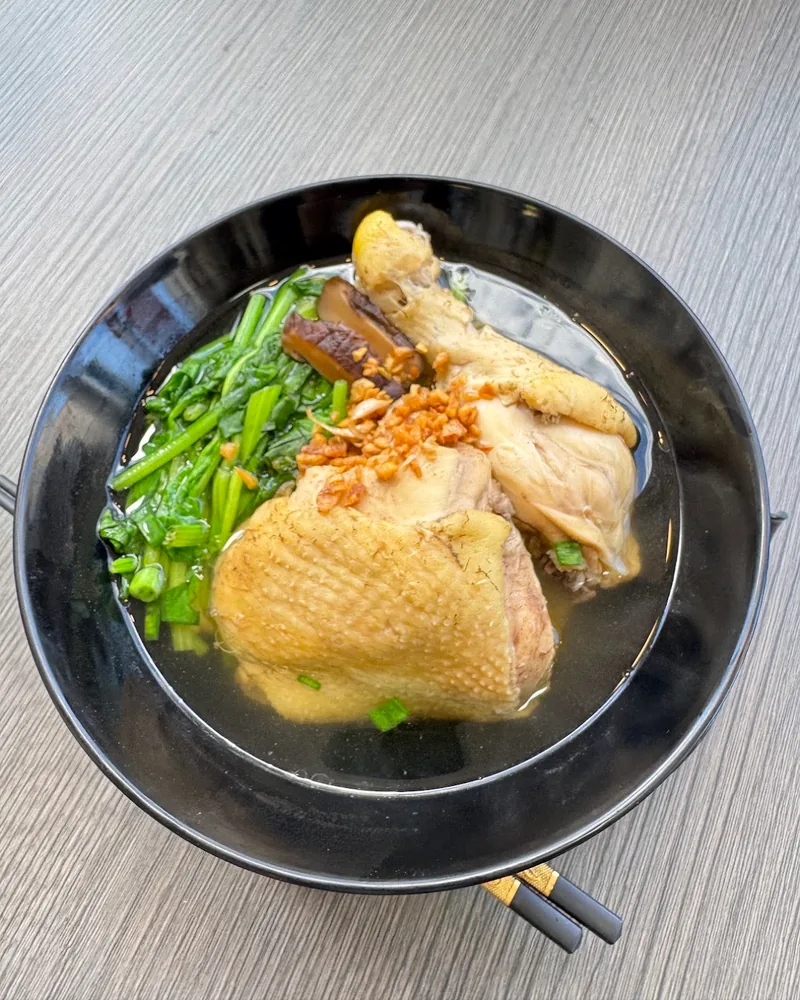 Chicken noodle soup with greens in a black bowl at The Noodle House