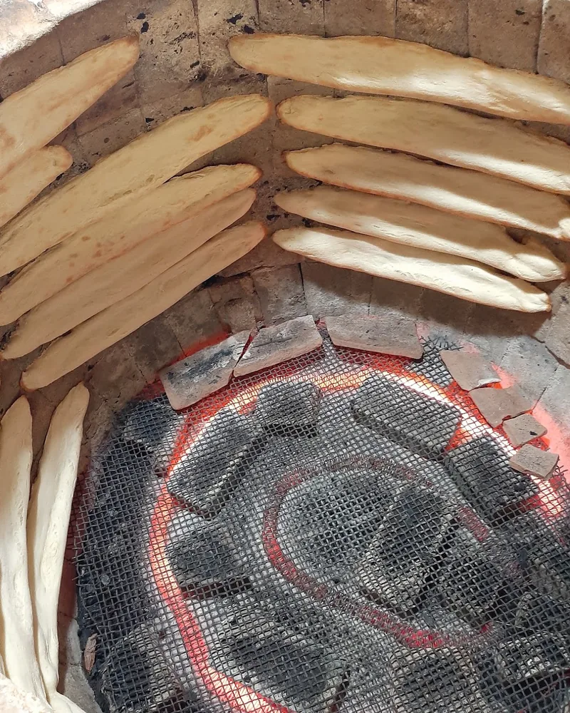 Long loaves of shotis puri stuck to the inside wall of a round clay tone oven above glowing coals at Tone (Georgian Bakery)