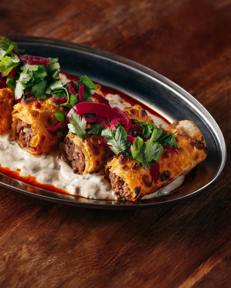 Meat rolls garnished with herbs on sauce in a metal platter at Tsiskvili Beer Square in Saburtalo