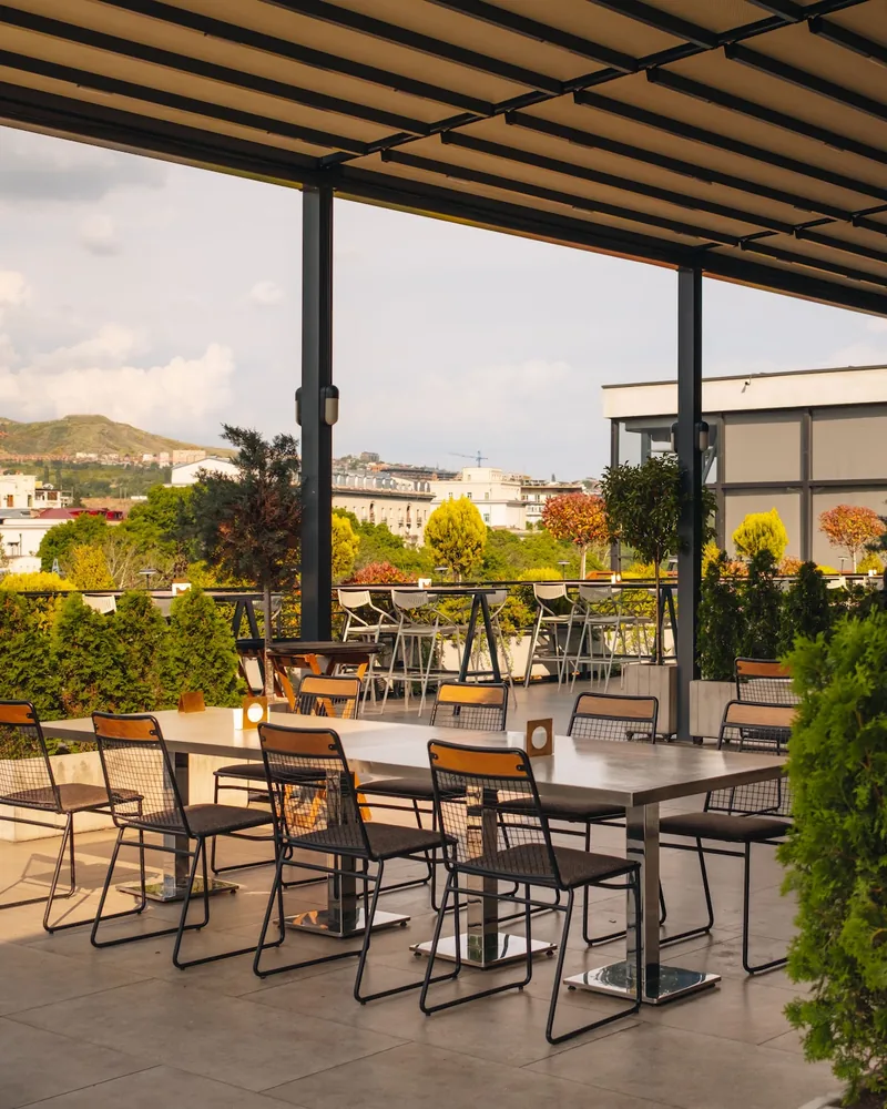 Covered rooftop terrace with outdoor dining tables and city view at Tsiskvili Terrace