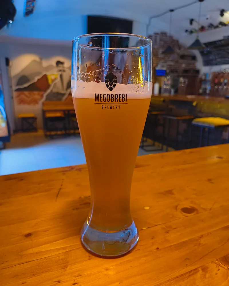 A tall glass of Megobrebi craft beer on a wooden counter at Tsota Tsota