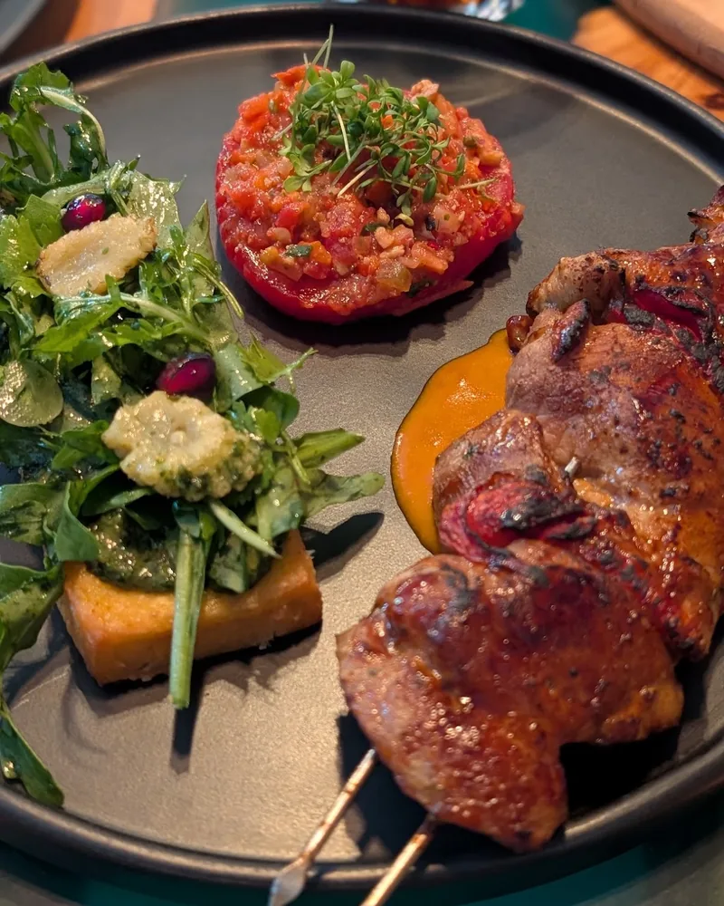 Chicken skewer with tomato tartare and herb salad on a black plate at Van Goghi