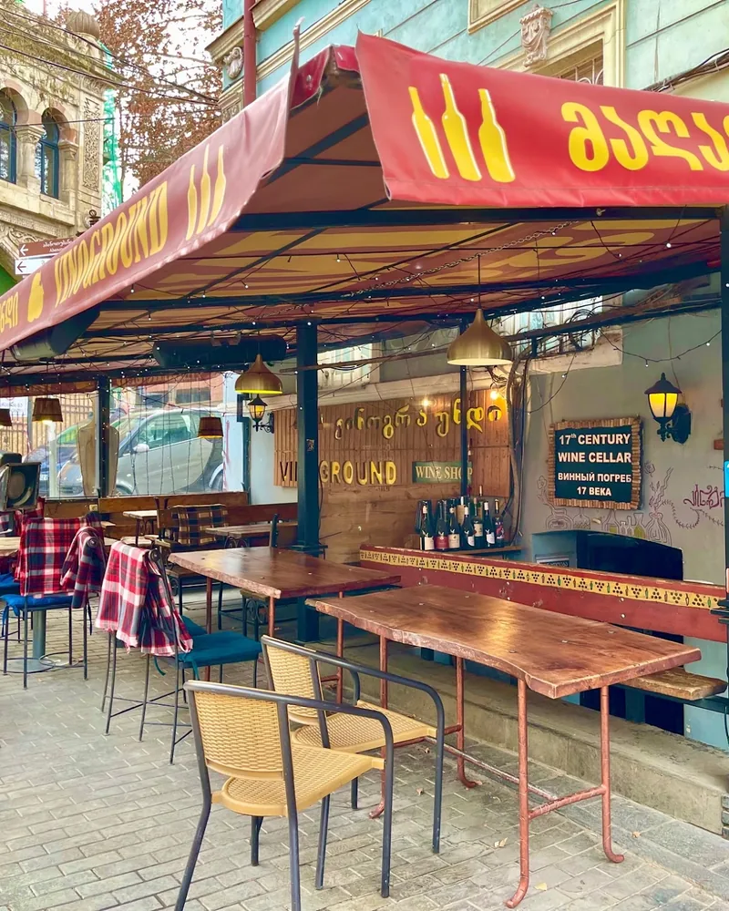 Covered outdoor terrace seating under a red awning at Vinoground
