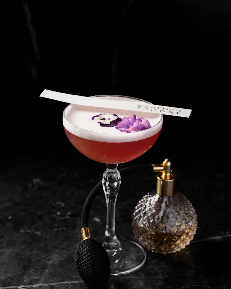 Cocktail in a coupe glass garnished with edible flowers at Weather Report Sky Bar