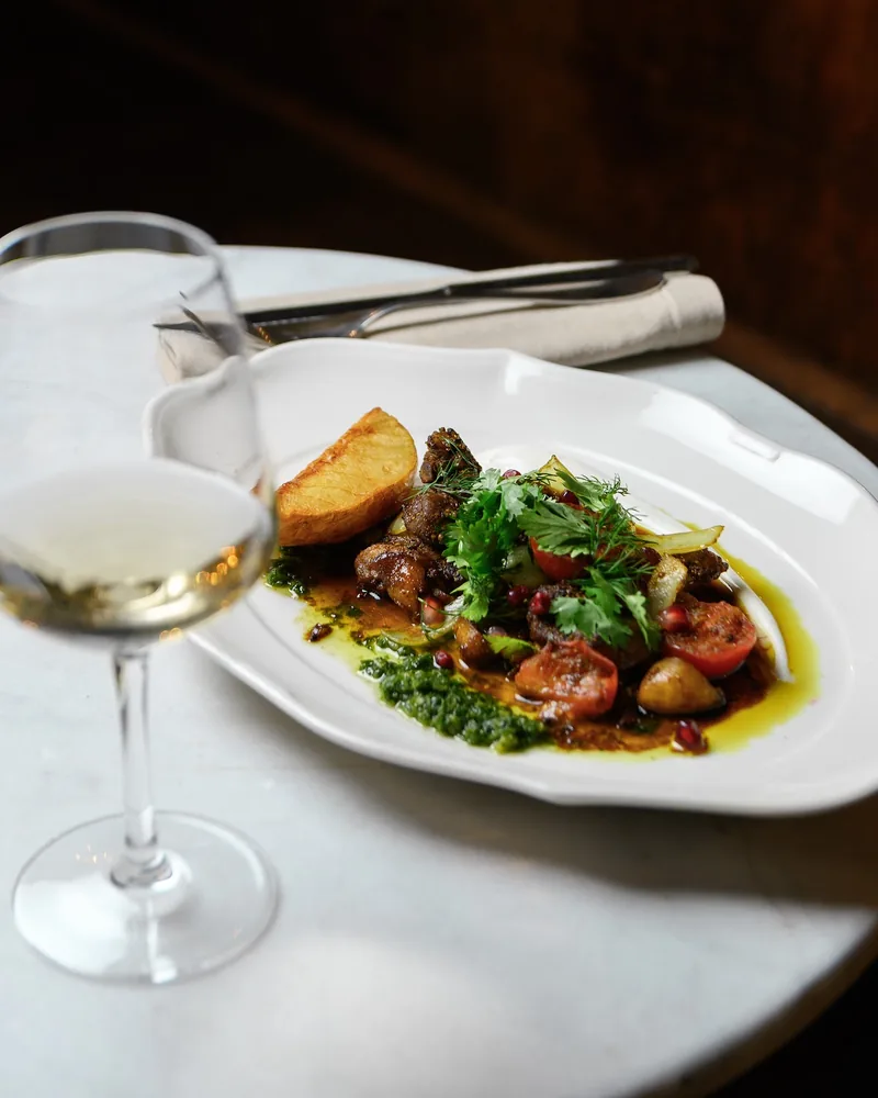 Roasted meat and vegetables on a white platter with white wine at Weller