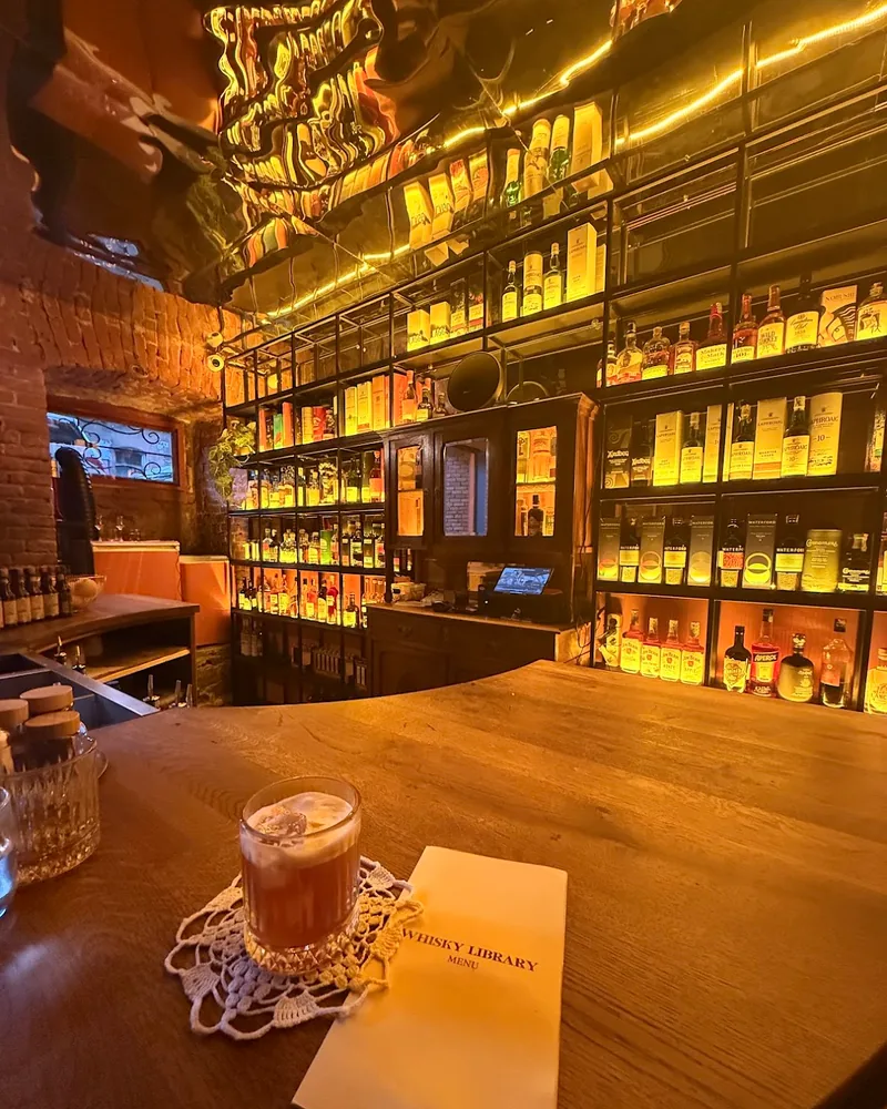 Wooden bar counter under illuminated bottle shelves at Whisky Library