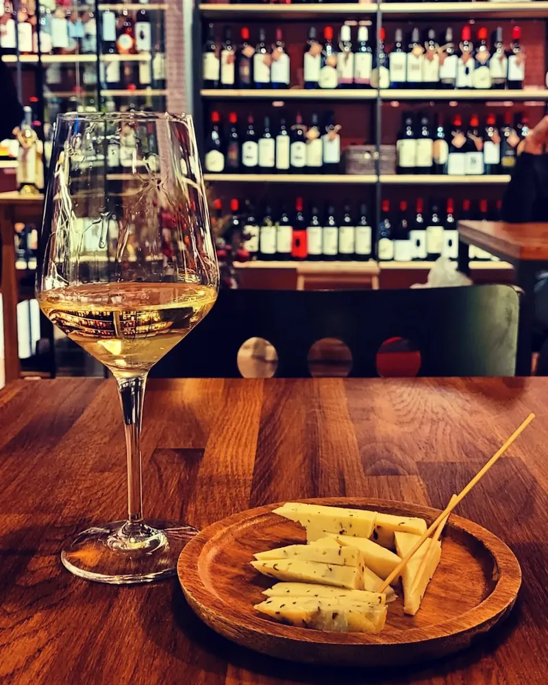 White wine in a wine glass with a wooden plate of sliced cheese at Wine Point