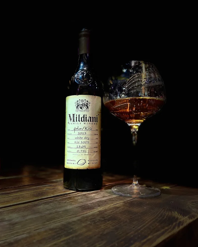 Glass of amber wine next to a bottle of Mildiani Kisi at Wine Tower