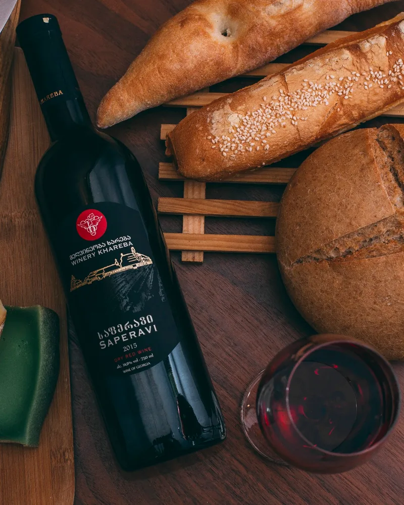 A bottle of dry Saperavi red lying beside loaves of bread and a glass of red wine at Winery Khareba