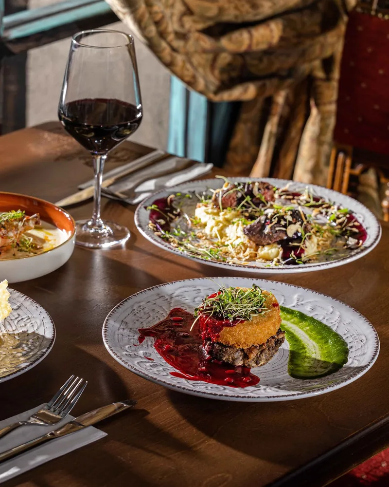 Table spread of plated modern Georgian dishes and red wine at Zala Restaurant & Cellar