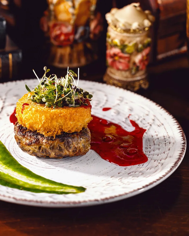Plated meat patty topped with fried cheese and microgreens at Zala Restaurant & Cellar